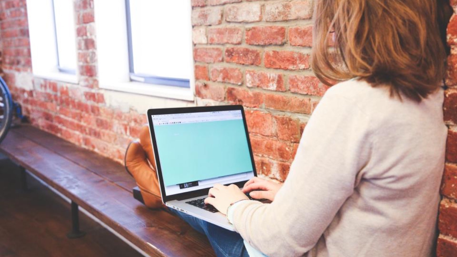 Mulher trabalhando em um notebook, sentada junto a uma parede de tijolos