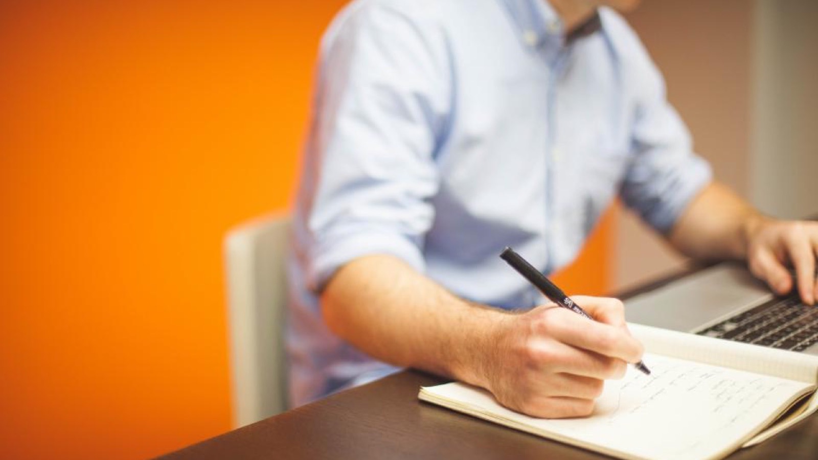 Pessoa escrevendo em um caderno sobre a mesa de trabalho
